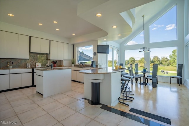 kitchen featuring white cabinetry, light tile patterned floors, a kitchen island with sink, and backsplash