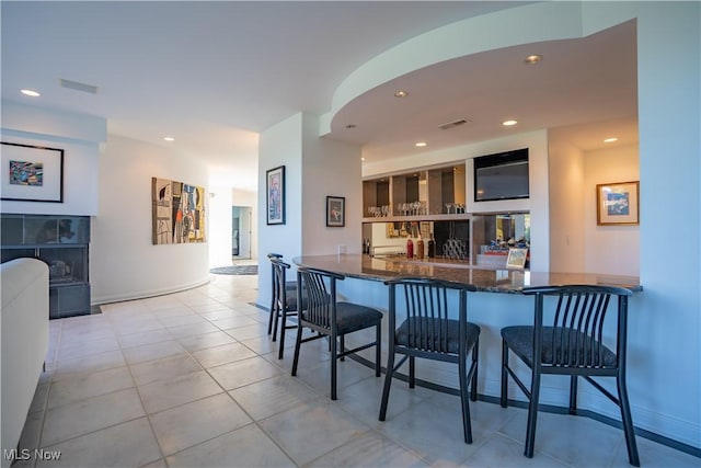 kitchen featuring light tile patterned floors, a fireplace, a kitchen bar, and kitchen peninsula