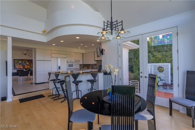 dining area featuring french doors, high vaulted ceiling, light hardwood / wood-style flooring, and a notable chandelier