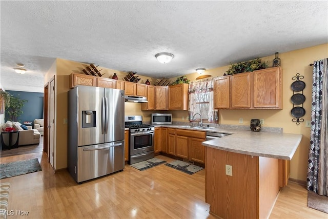 kitchen featuring sink, a textured ceiling, appliances with stainless steel finishes, kitchen peninsula, and light hardwood / wood-style floors