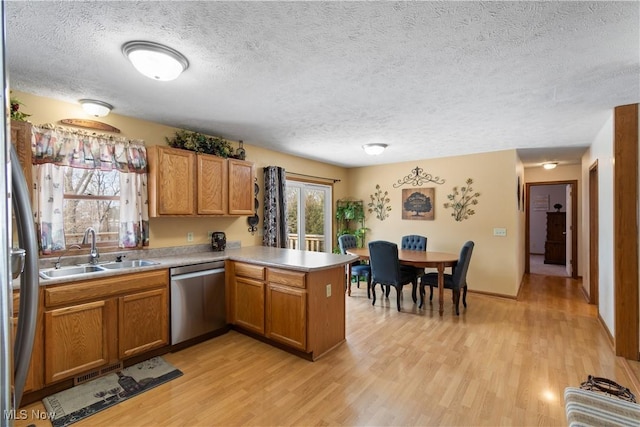 kitchen featuring sink, light wood-type flooring, stainless steel dishwasher, kitchen peninsula, and a textured ceiling