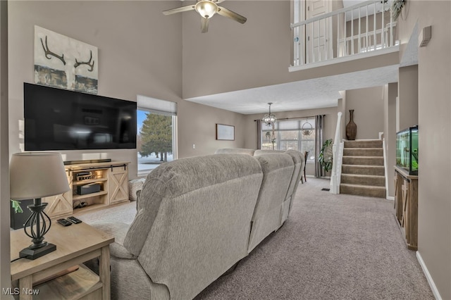 carpeted living room with ceiling fan with notable chandelier and a high ceiling