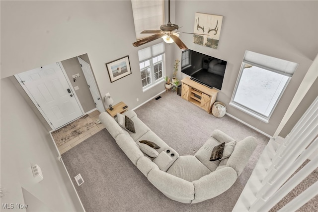 living room featuring ceiling fan, carpet floors, and a towering ceiling