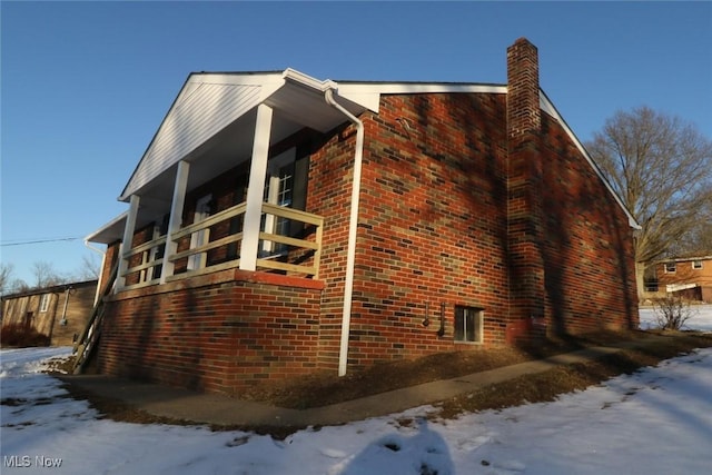 snow covered property featuring a chimney and brick siding