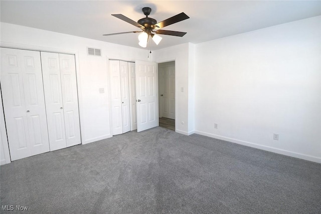 unfurnished bedroom featuring multiple closets, dark carpet, and ceiling fan