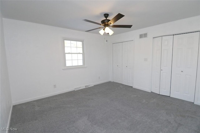 unfurnished bedroom featuring multiple closets, dark carpet, and ceiling fan