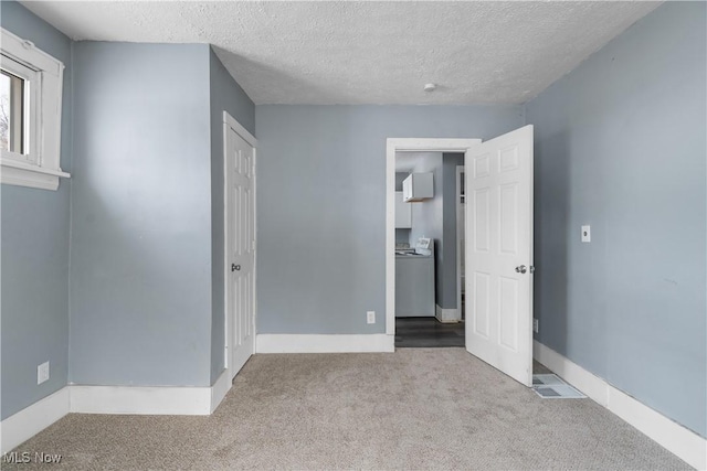 unfurnished bedroom featuring washer / clothes dryer, light colored carpet, and a textured ceiling