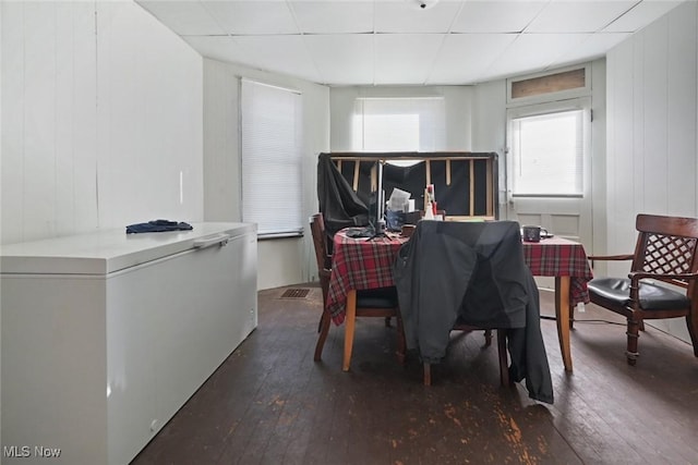 dining space with wooden walls, a drop ceiling, and dark hardwood / wood-style flooring