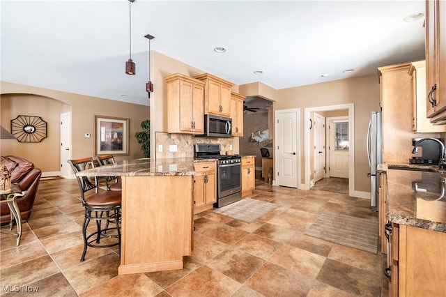 kitchen with appliances with stainless steel finishes, stone countertops, and light brown cabinetry