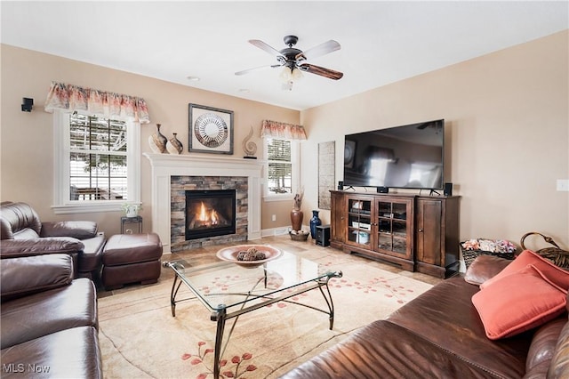 living room featuring light tile patterned flooring, ceiling fan, a stone fireplace, and a wealth of natural light