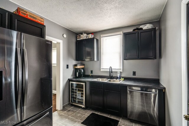 kitchen with wine cooler, sink, a textured ceiling, appliances with stainless steel finishes, and tile patterned flooring