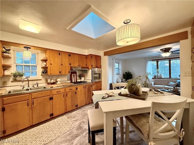 kitchen with a skylight, oven, sink, and stainless steel counters