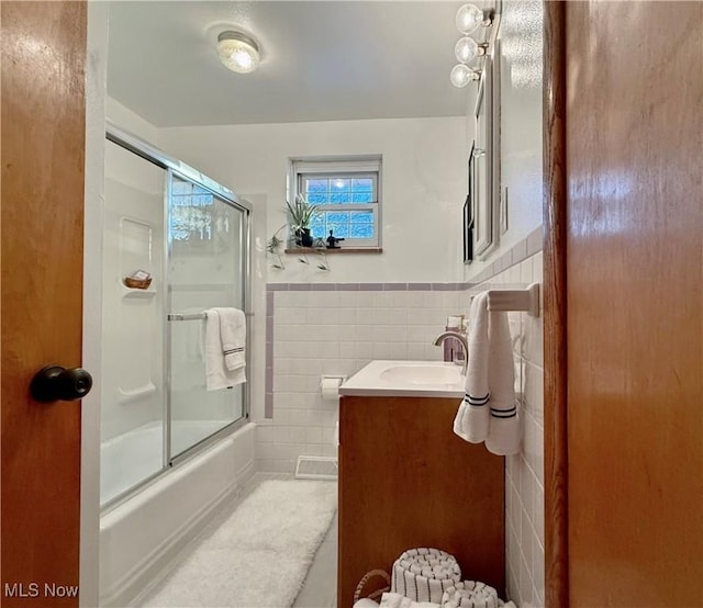 full bathroom with vanity, tile walls, wainscoting, and enclosed tub / shower combo