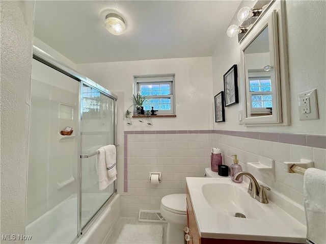 full bath featuring visible vents, toilet, vanity, shower / bath combination with glass door, and tile walls