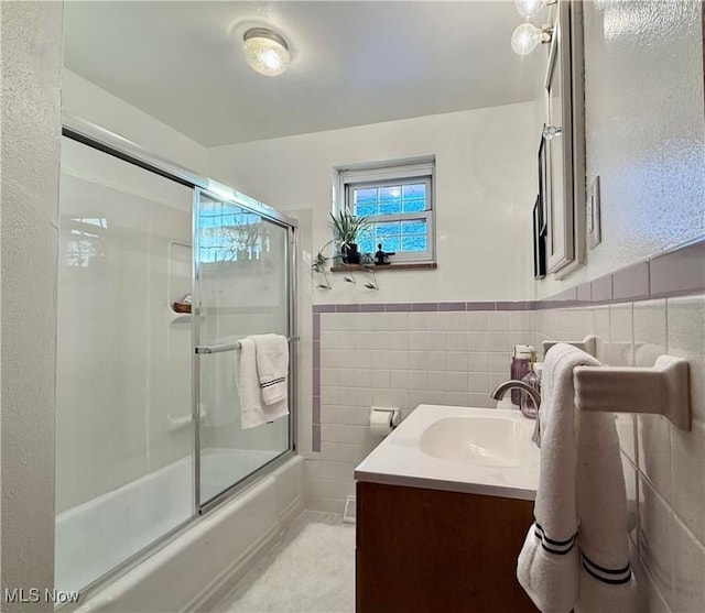 full bath with a wainscoted wall, shower / bath combination with glass door, tile walls, and vanity