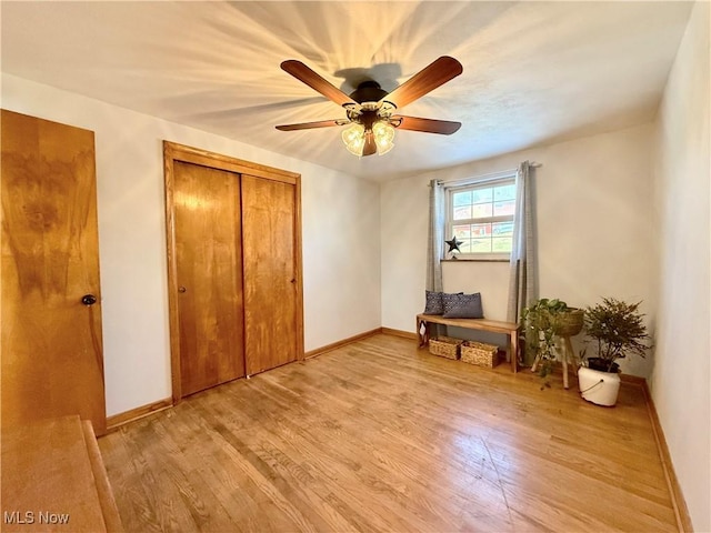 interior space featuring a closet, light wood-style flooring, a ceiling fan, and baseboards