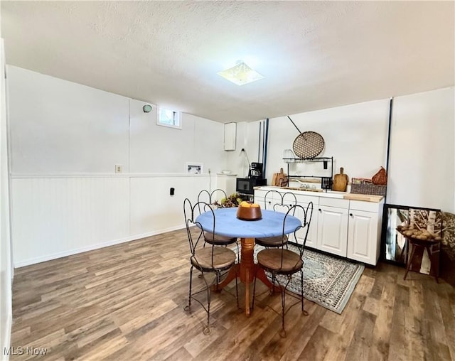 dining room with a wainscoted wall, a textured ceiling, and wood finished floors