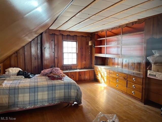 bedroom with lofted ceiling, hardwood / wood-style floors, and wooden walls