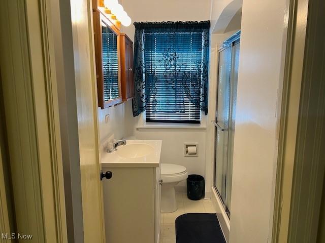 bathroom featuring tile patterned flooring, vanity, a shower with shower door, and toilet