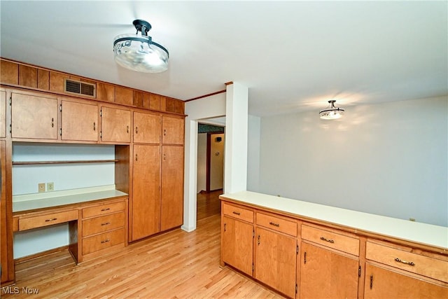 kitchen with ornamental molding, built in desk, and light hardwood / wood-style floors