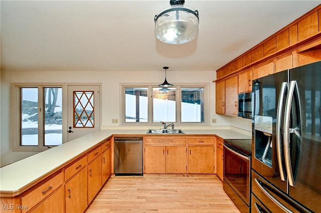 kitchen featuring sink, decorative light fixtures, kitchen peninsula, light hardwood / wood-style floors, and black appliances