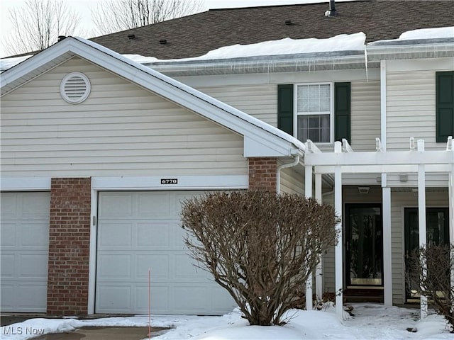 snow covered property featuring a pergola and a garage