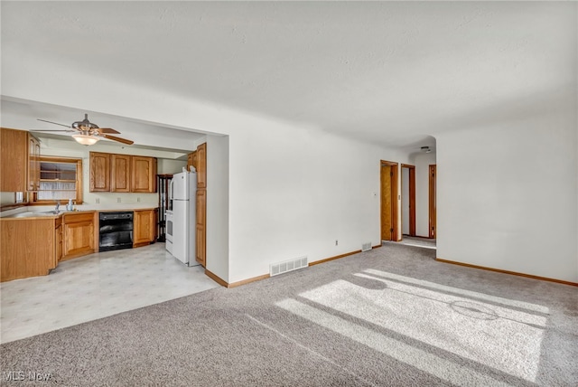 unfurnished living room with sink, light colored carpet, and ceiling fan