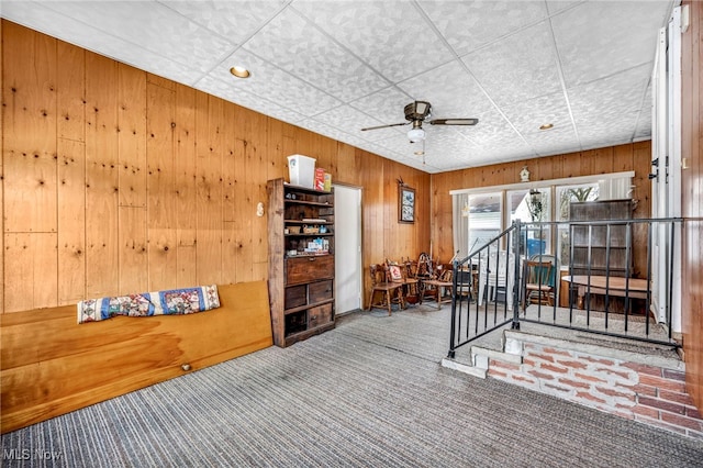 interior space with wooden walls, ceiling fan, and carpet flooring