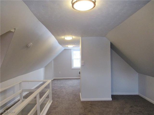 additional living space with dark colored carpet, vaulted ceiling, and a textured ceiling