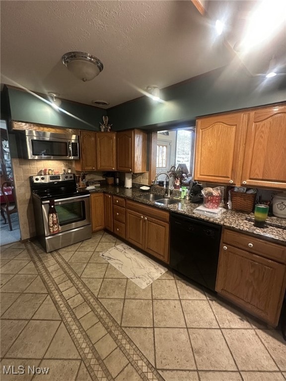 kitchen with appliances with stainless steel finishes, sink, light tile patterned floors, and dark stone counters