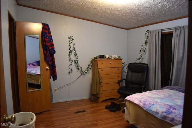 bedroom featuring wood-type flooring, ornamental molding, and a textured ceiling