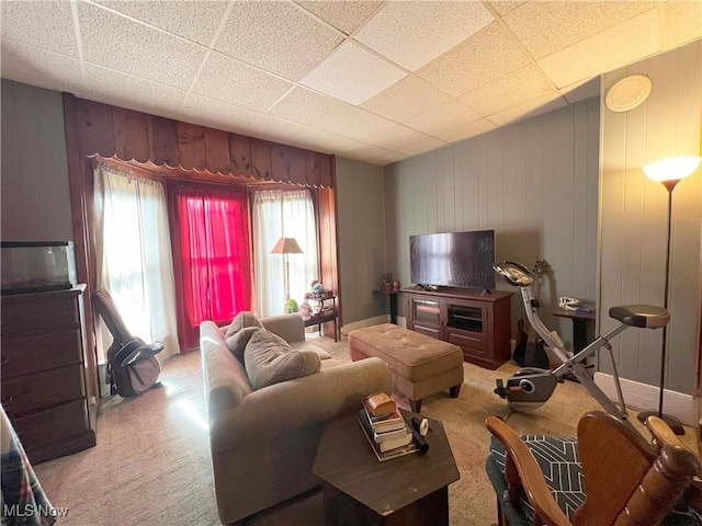 carpeted living room with a drop ceiling and wood walls