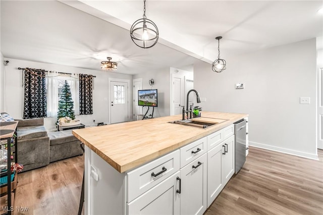 kitchen featuring a kitchen island with sink, hanging light fixtures, sink, and butcher block counters