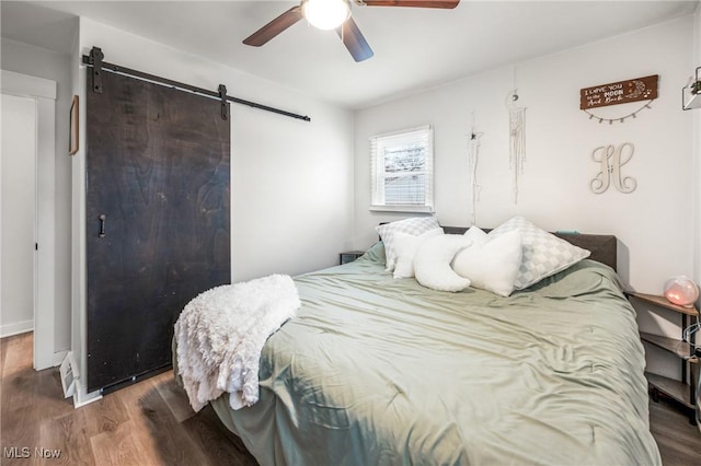 bedroom featuring hardwood / wood-style flooring, a barn door, and ceiling fan