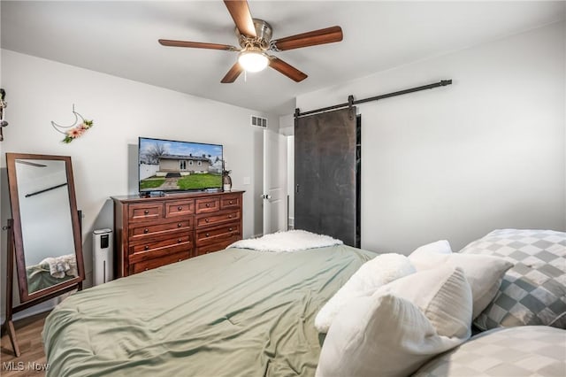 bedroom featuring hardwood / wood-style floors, a barn door, and ceiling fan