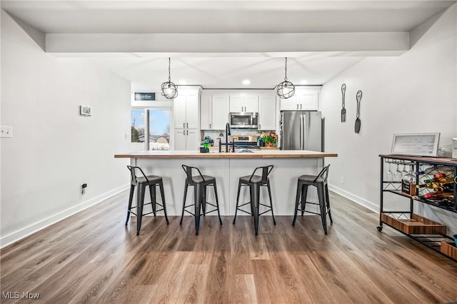 kitchen featuring a breakfast bar, tasteful backsplash, hanging light fixtures, appliances with stainless steel finishes, and white cabinets