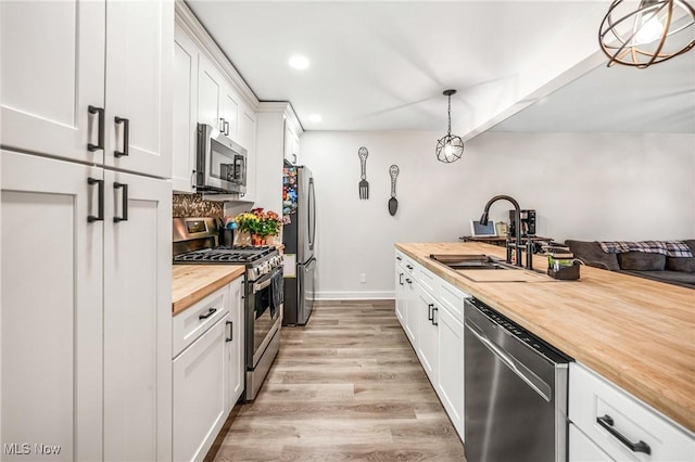 kitchen featuring butcher block countertops, sink, appliances with stainless steel finishes, hanging light fixtures, and white cabinets