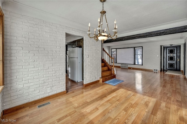 unfurnished dining area with hardwood / wood-style flooring, brick wall, an inviting chandelier, and a textured ceiling