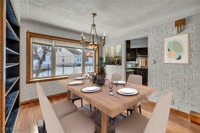 dining space with brick wall, a notable chandelier, a textured ceiling, and light hardwood / wood-style flooring