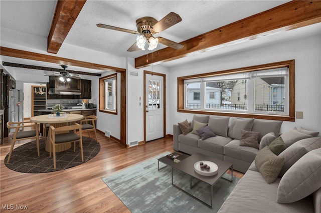 living room featuring beamed ceiling, ceiling fan, light hardwood / wood-style flooring, and a textured ceiling