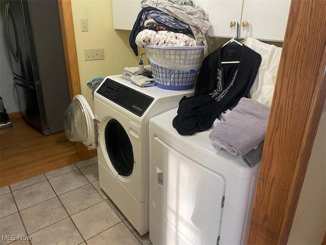 clothes washing area featuring cabinets, light tile patterned floors, and washing machine and clothes dryer