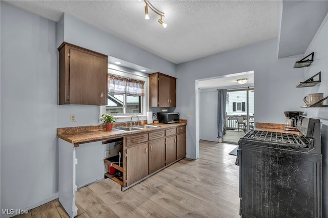 kitchen featuring sink, light wood-type flooring, black range with gas stovetop, dark brown cabinetry, and a textured ceiling