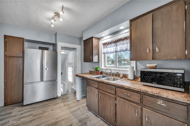 kitchen featuring sink, light hardwood / wood-style flooring, dark brown cabinets, stainless steel appliances, and a textured ceiling