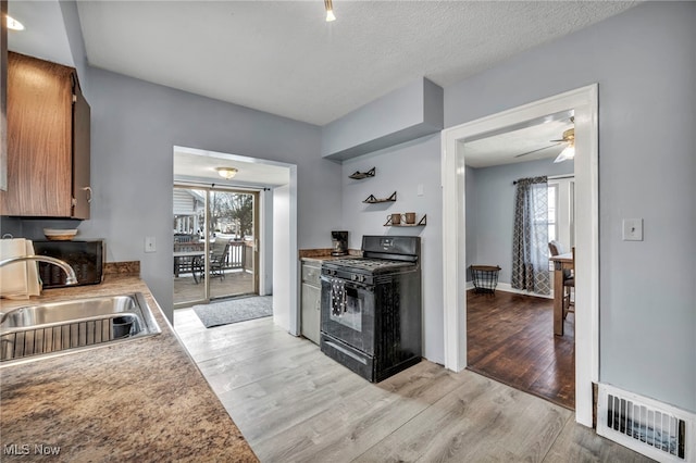 kitchen with black range with gas stovetop, sink, light hardwood / wood-style flooring, and a textured ceiling