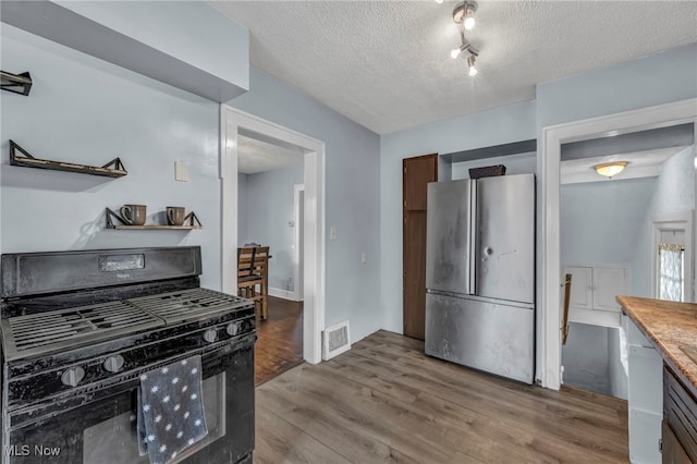 kitchen featuring black gas range oven, stainless steel refrigerator, dishwasher, wood-type flooring, and a textured ceiling