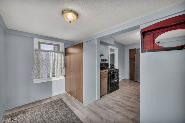 kitchen featuring stainless steel fridge, black range with gas stovetop, a textured ceiling, and light hardwood / wood-style flooring