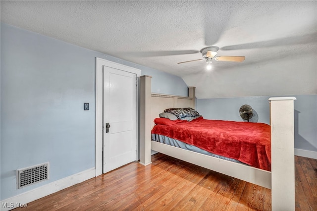 bedroom with hardwood / wood-style flooring, ceiling fan, vaulted ceiling, and a textured ceiling