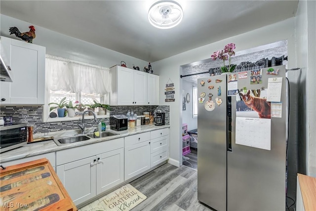 kitchen with stainless steel refrigerator, sink, white cabinets, decorative backsplash, and light hardwood / wood-style flooring