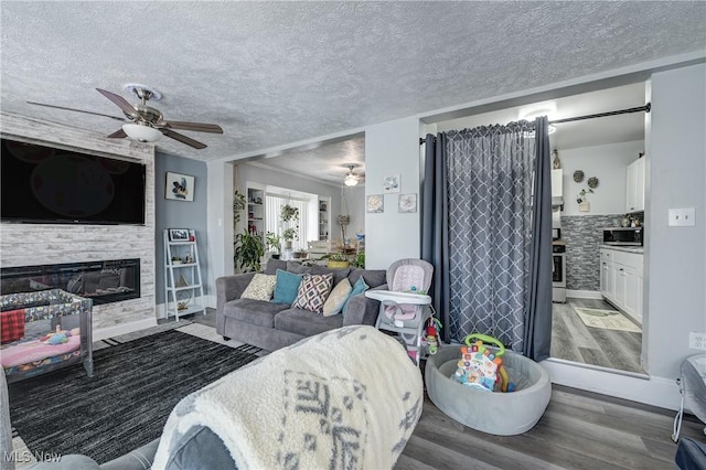 living room with ceiling fan, dark wood-type flooring, a large fireplace, and a textured ceiling