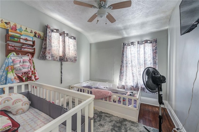 bedroom featuring ceiling fan, vaulted ceiling, a textured ceiling, and a crib